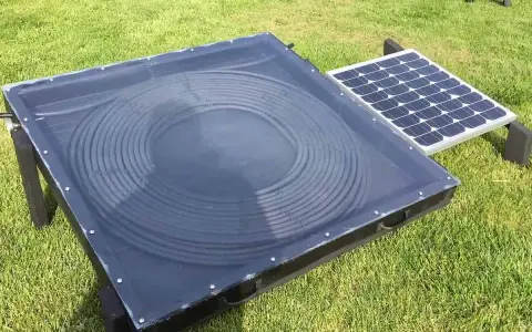 Un système de chauffage air solaire avec un panneau de tubes noirs en spirale sous une couverture transparente, à côté d'un petit panneau solaire.