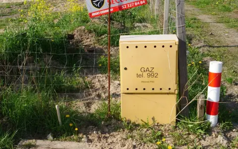 Żółta skrzynka gazowa z napisem "GAZ tel. 992" stoi obok ogrodzenia. Czy skrzynka gazowa musi być żółta?