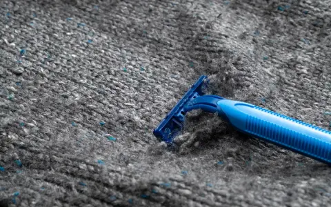 En blå rakhyvel tar bort noppor från en grå stickad tröja i polyester.