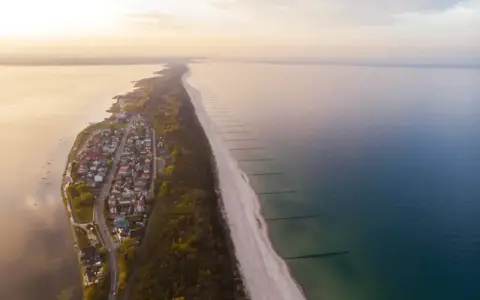 Widok z lotu ptaka na malownicze chałupy nad morzem, z piaszczystą plażą i spokojną wodą.