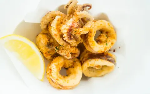 Crujientes calamares a la andaluza, dorados y sazonados, servidos con una rodaja de limón fresco.
