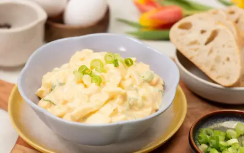 Cremiger Eiersalat mit Joghurt und Gurke, garniert mit Frühlingszwiebeln, serviert mit Brot.