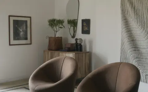 Två bruna fåtöljer framför en träbyrå med spegel och konst. En inredningsdröm inspirerad av Marie Olsson Nylander för Ellos.