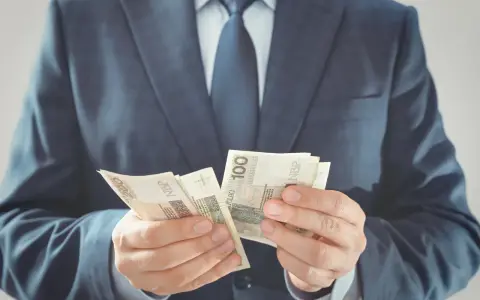 Mężczyzna w garniturze liczy banknoty 100 zł. To jego zabezpieczenie finansowe na przyszłość.