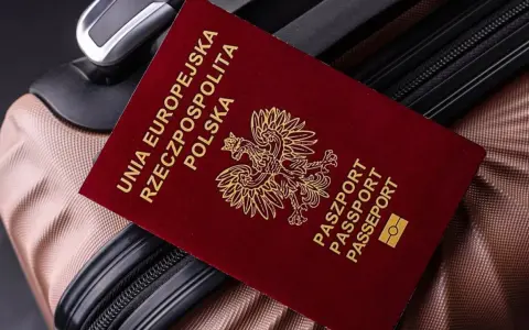 Czerwony paszport Polski z godłem orła leży na brązowej walizce.