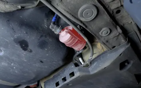 El filtro de combustible, de color rojo y transparente, está ubicado debajo del coche, cerca del tanque.