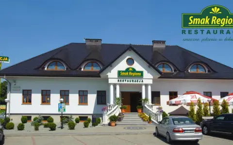 Restauracja "Smak Regionu" z białym budynkiem, schodami i samochodami na parkingu.