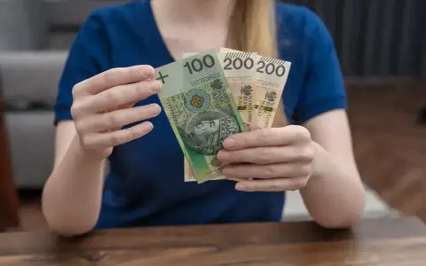 Kobieta trzyma polskie banknoty 100 i 200 zł. Zastanawia się, urlop macierzyński ile płatny.