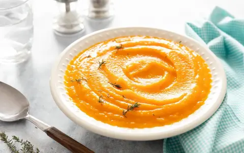 Un bol de velouté de purée de butternut, garni de thym frais, prêt à être dégusté avec une cuillère en argent.