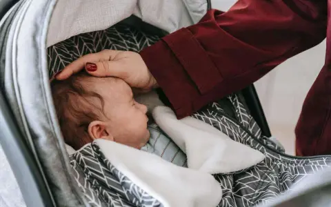 Delikatna dłoń głaszcze śpiące dziecko w wózku. Nawet podczas regresu snu u rocznego dziecka, czułość rodzica przynosi ukojenie.