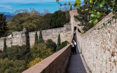 Spaziergang auf der Stadtmauer von Girona, Spanien. Zwei Frauen genießen die Aussicht auf die historische Festung und die grüne Landschaft.