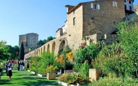 Jardin luxuriant devant le **château de Lauris**, avec ses murs de pierre et ses arches médiévales.