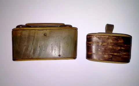 Dwie zabytkowe tabakiery z rogu, jedna z wygrawerowanymi sercami, druga z ozdobnym, drewnianym wzorem.