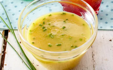 Ein Glas mit cremigem honig senf dressing, garniert mit Schnittlauch. Perfekt für einen frischen Salat.