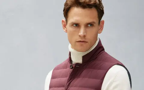 Uomo con gilet imbottito bordeaux sopra dolcevita bianco. Il gilet, un capo versatile, aggiunge stile e calore.