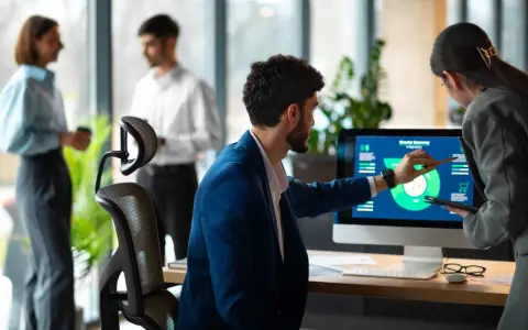 Uomini e donne discutono di grafici su un monitor, esplorando nuove opportunità di lavori del futuro senza laurea.