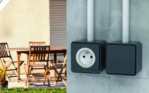 Branchement prise extérieur sur mur de béton. Une prise électrique noire est visible, avec une autre à côté. Une table et des chaises en bois sont sur une terrasse.