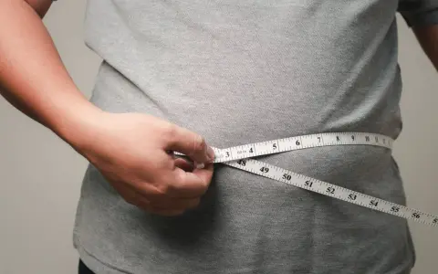 Eine Hand misst mit einem Maßband die Taille. Viele fragen sich, wo nimmt man zuerst ab – oft ist es der Bauch.
