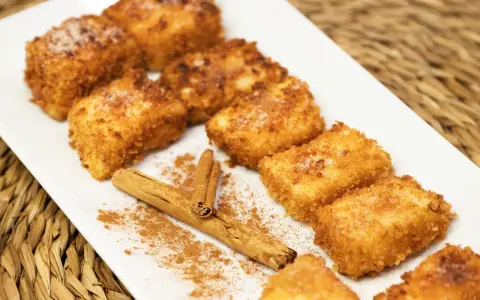 Deliciosa leche frita dorada y crujiente, espolvoreada con azúcar y canela, junto a una rama de canela.