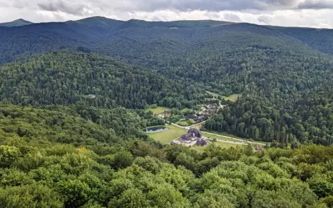 Widok z tarasu widokowego Bieszczady na zieloną dolinę z jeziorem i zabudowaniami.