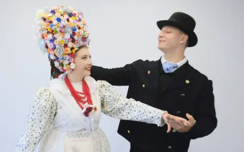 Para tańczy w strojach ludowych, co to folklor. Ona ma bogato zdobiony kwiatami wianek, on czarny kapelusz i marynarkę.