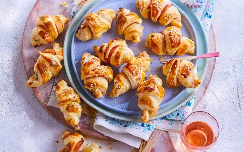 Petits croissants au jambon dorés, certains saupoudrés de graines de sésame ou de pavot, prêts à être dégustés.
