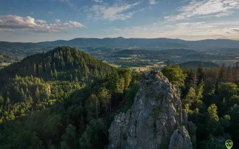 Widok na skalne formacje Rudawy Janowickie, porośnięte lasem, z ludźmi na szczycie. W tle rozległa panorama gór i dolin.