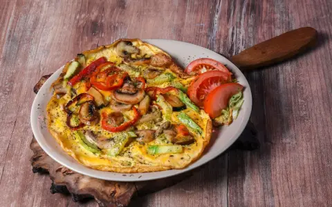 Pyszny omlet z pieczarkami, papryką i cukinią, udekorowany pomidorem i sałatą.