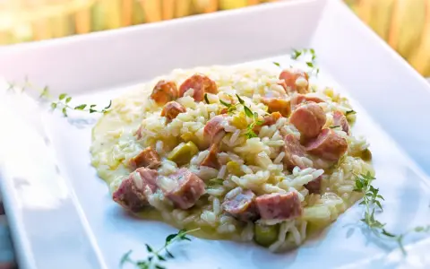 Un cremoso risotto con salsiccia, piselli e timo, servito su un piatto bianco.