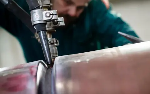 Saldatore esperto esegue saldatura ad arco sommerso su un tubo metallico, creando un giunto robusto.