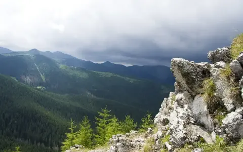 Skalisty szczyt w Zakopanem z widokiem na gęsto zalesione doliny Tatr pod burzowym niebem.