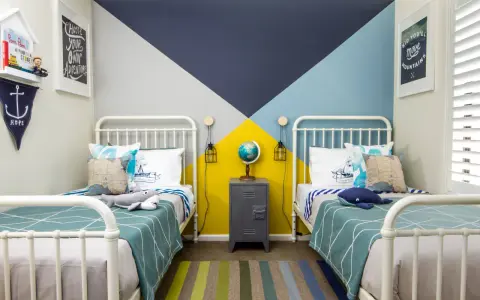 Habitaciones juveniles con camas blancas y pared geométrica en azul, gris y amarillo. Alfombra de rayas y decoración náutica.