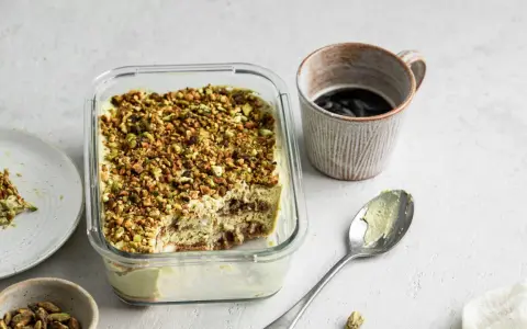 Un delizioso tiramisù al pistacchio, cosparso di granella verde, pronto per essere gustato con un caffè.
