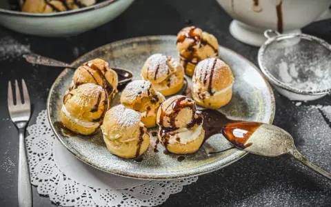 Köstliche Profiteroles, bestäubt mit Puderzucker und beträufelt mit Schokoladensauce. Ein wahrer Genuss, wie beim original profiteroles rezept.