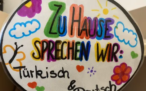 Bunte Zeichnung mit der Aufschrift "Zu Hause sprechen wir: Türkisch & Deutsch". Ein Beispiel für vorurteilsbewusste Pädagogik, die Mehrsprachigkeit feiert.