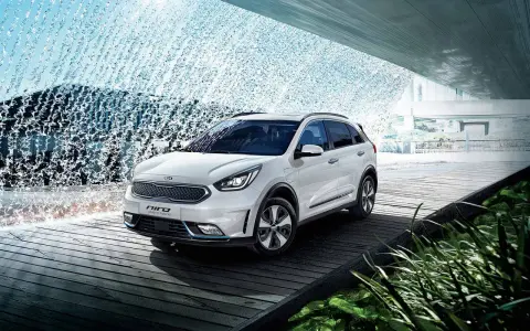 Biały Kia Niro Plug-in Hybrid na drewnianej platformie, otoczony wodnymi kaskadami i zielenią.
