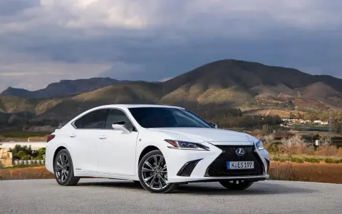 Biały Lexus ES 300h zaparkowany na tle górskiego krajobrazu. Elegancki sedan prezentuje się okazale na tle natury.