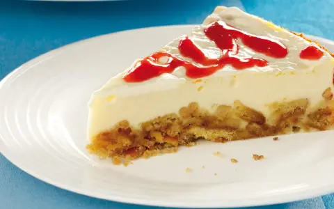 Ein Stück cremiger cheesecake mit keksboden, garniert mit rotem Fruchtpüree auf einem weißen Teller.
