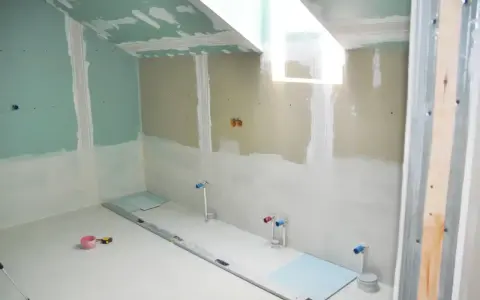 Chantier de salle de bain : murs en plaques de plâtre, tuyauterie apparente, niveau à bulle et outils au sol. Travaux d'isolation salle de bain en cours.
