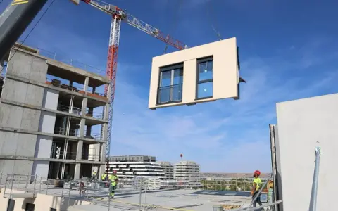 Grúa elevando un módulo prefabricado para la construcción industrializada de un edificio. Obreros supervisan la operación.
