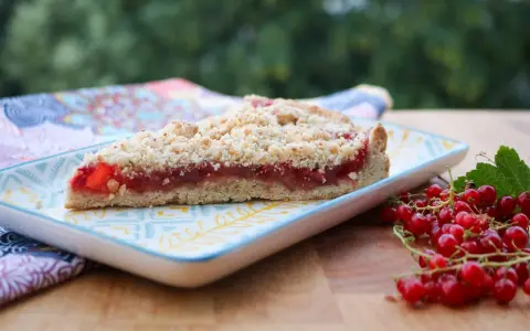 Ein Stück saftiger Johannisbeer Streuselkuchen mit frischen roten Johannisbeeren daneben.