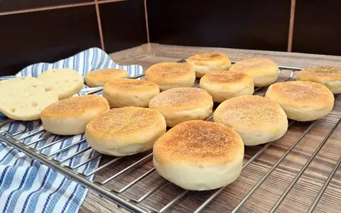 Świeżo upieczone muffiny angielskie, lekko zrumienione, czekają na śniadanie. Dwa przekrojone bułeczki odsłaniają puszyste wnętrze.