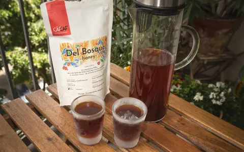 Kalter Kaffee in Gläsern auf Holztisch. Daneben eine Karaffe mit Kaffee und eine Packung "Del Bosque honey". Ein kühler Genuss an einem warmen Tag.