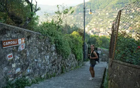Una ragazza con zaino su un sentiero panoramico, con un cartello che indica Camogli. Perfetto per chi cerca dove dormire sul Cammino del Tigullio.