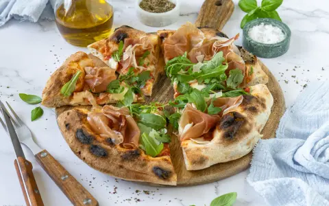 Pizza mit Prosciutto, Rucola und frisch gehobeltem Parmesan. Ein Genuss für alle Sinne!