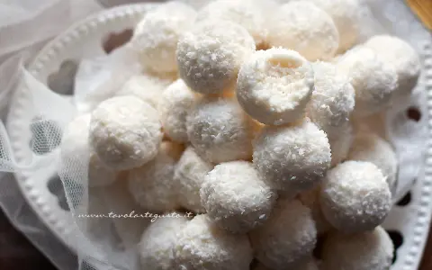 Dolci palline di cocco, morbide e profumate, adagiate su un piatto decorato con un velo di tulle.