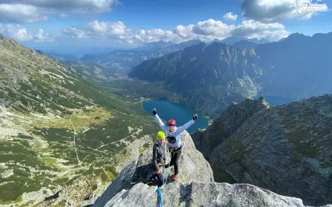 Dwóch wspinaczy na szczycie, z widokiem na Tatry i Morskie Oko. W tle góry i jezioro.