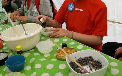 Dzieci w przedszkolu uczą się, jak zrobić mydło, dodając składniki do foremek.