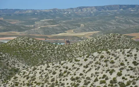 Paisaje árido del desierto de Monegros con colinas cubiertas de matorral y una torre de iglesia solitaria al fondo.