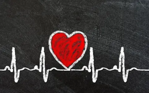 Czerwone serce na tle EKG symbolizuje zagrożenia dla zdrowia serca, w tym skutki otyłości u mężczyzn.